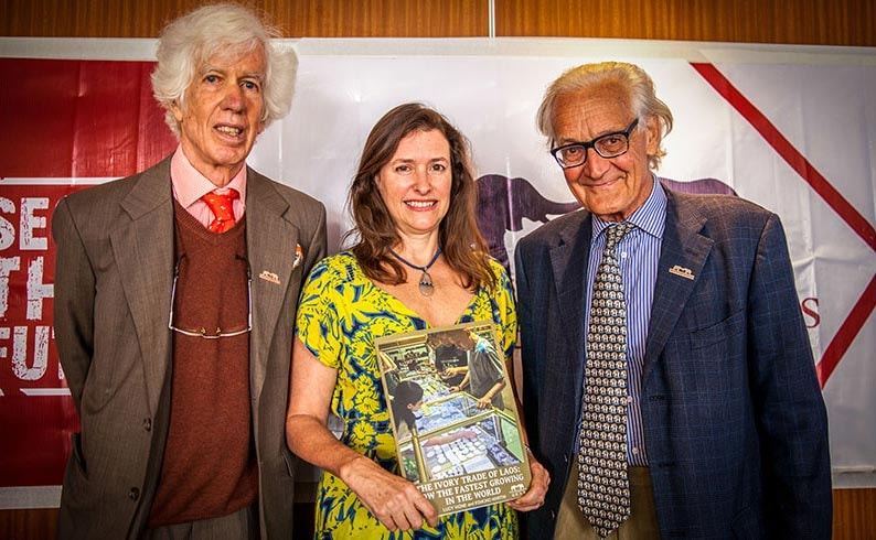 A woman holding a book stands between two men.