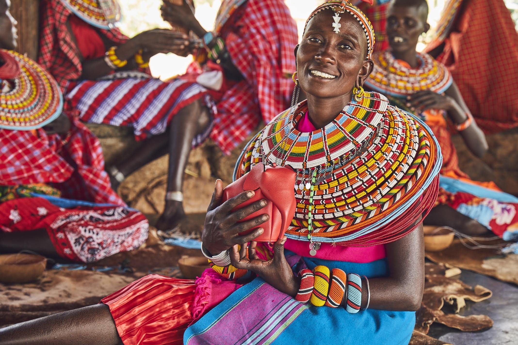 Seated woman wearing beaded jewellery holds small elephant shaped bag
